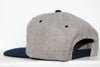 Side view of a gray and navy Wichita Wind snapback hat with adjustable strap on white surface